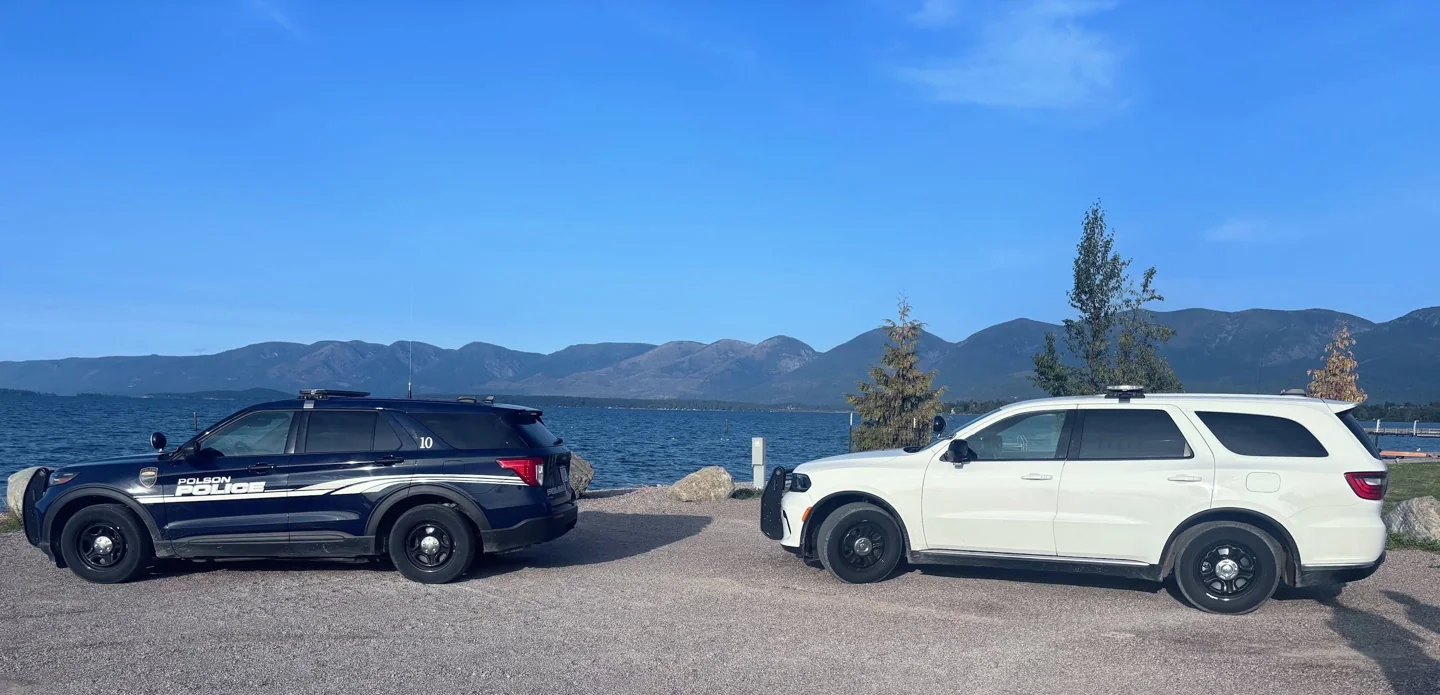 Two Polson Police SUVs beside Flathead Lake with mountains in the background